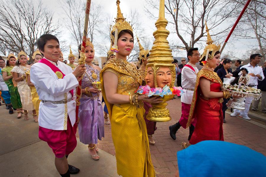 An Asian woman dressed in gold walks in a procession during a Khmer New Year celebration.