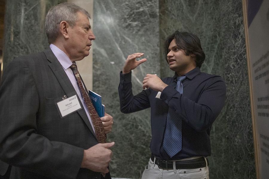 A business analytics student speaks to a senator in front of a green marble background.