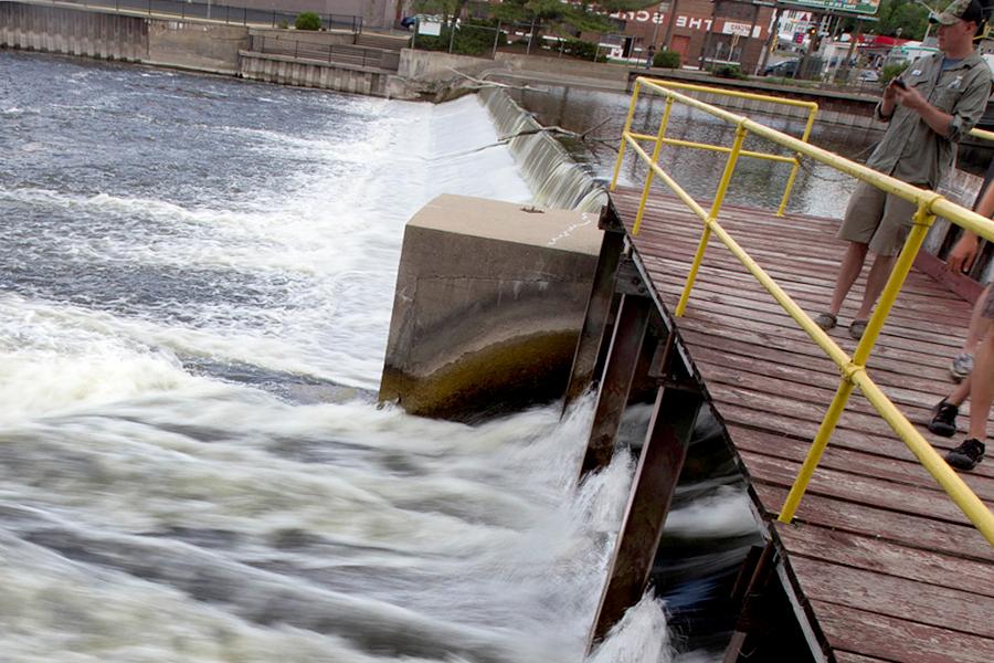 A student stands on a pier with a water testing device as water rushes underneath.