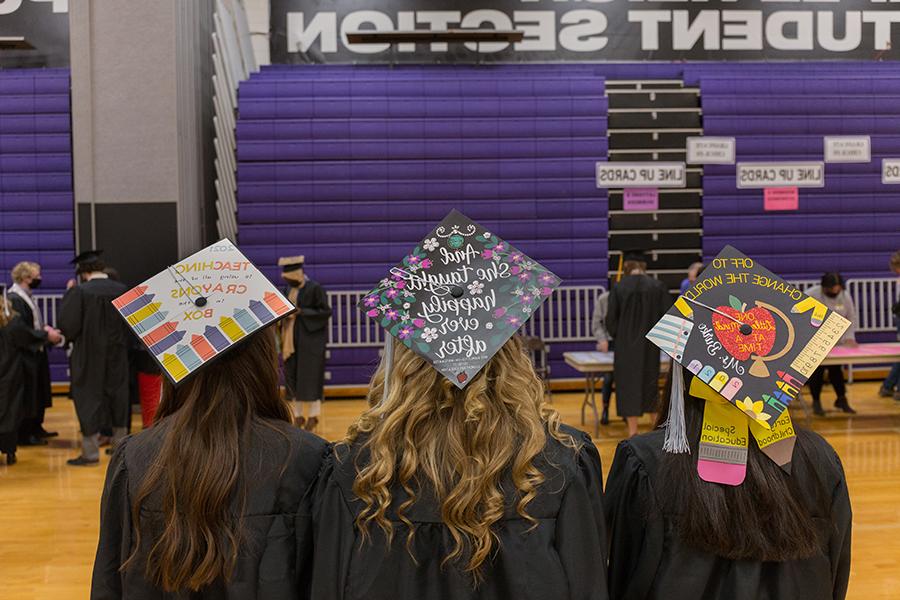 Three education majors show their decorated caps at graduation.